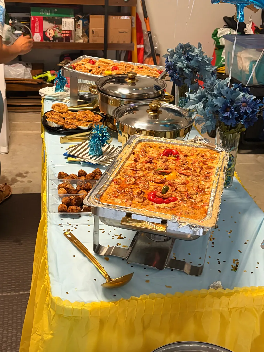A Bayou Fork Kitchen brunch buffet with Creole shrimp and grits, waffles and chafing dishes on a blue and gold table